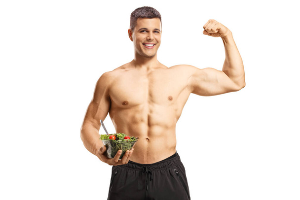 Shirtless musuclar man holding a salad and flexing muscle isolated on white background - Fotó, kép