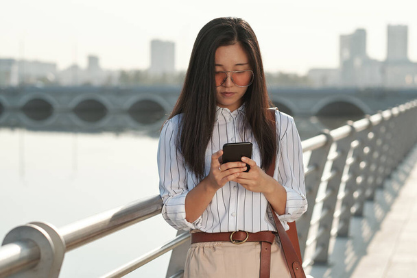 Jonge zakenvrouw scrollen in smartphone in stedelijke omgeving - Foto, afbeelding