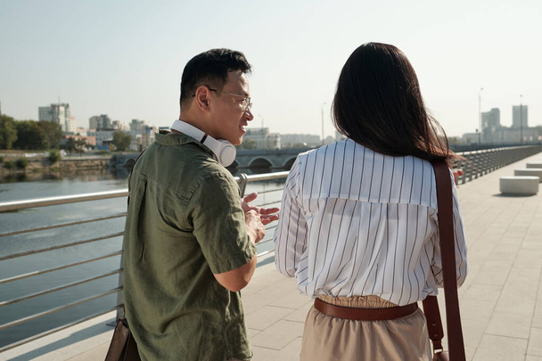 Rückansicht zweier junger chinesischer Kollegen, die spazieren gehen und interagieren - Foto, Bild