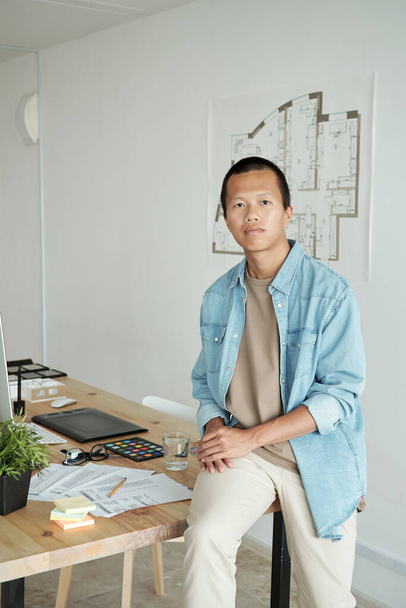 Çağdaş genç mimar masada duvardaki çizime karşı oturuyor. - Fotoğraf, Görsel