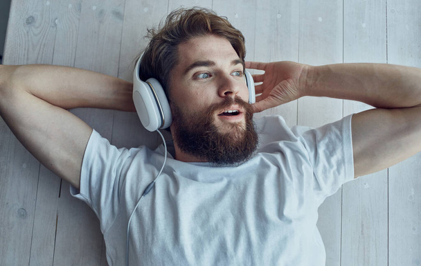 Mann hört Musik in weißen Kopfhörern am Fenster auf der Fensterbank - Foto, Bild