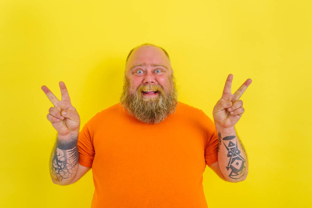 Homme heureux avec barbe et tatouages fait un geste gagnant avec les mains - Photo, image