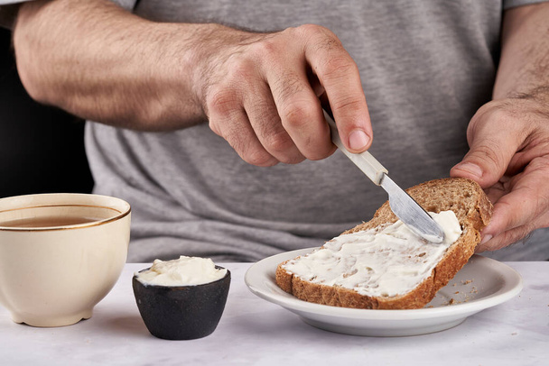 man's hands smearing cream cheese on slice of bran bread for breakfast - Foto, afbeelding