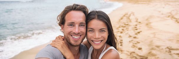 Tourists on beach Smiling beautiful young multiracial couple taking selfie on vacation panoramic banner crop. Asian woman, Caucasian man - Фото, изображение