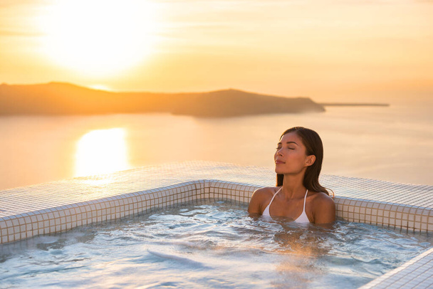 Spa hotel luxury relax jacuzzi therapy pool Asian woman relaxing in resort hot tub outside on private room balcony sunset over sea. Europe honeymoon vacation relaxation wellness pampering. - Foto, Bild