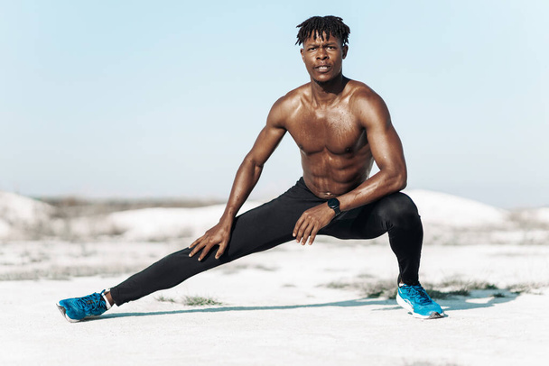 Handsome dark-skinned man, athlete doing leg stretching exercise after training outdoors in nature, sport concept, motivation, healthy lifestyle - Фото, зображення