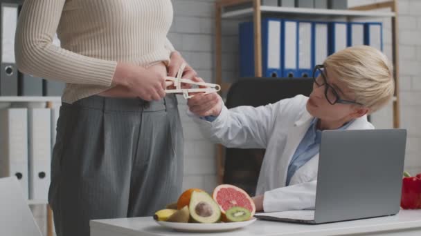 Arzt Ernährungsberater misst Körperfettindex für junge Patientin, bevor er Behandlungsplan aufstellt, sitzt im Büro - Filmmaterial, Video