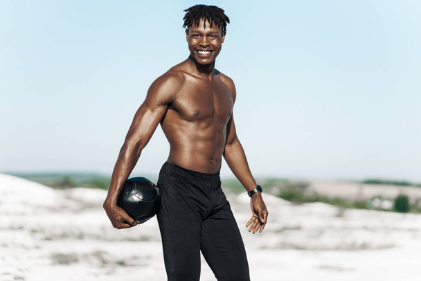 African American crossfit man, holding ball over head for shoulder press workout, outdoors against mountains background, muscular athlete doing upper body workout working out with heavy weighted balls - Foto, Bild