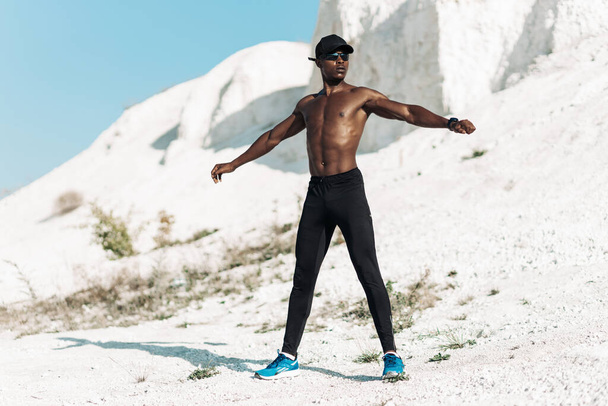 Muscular African American man doing stretching and getting ready for training and running outdoors in the mountains, Amazing mountain view in the background, Adventure sports concept - Photo, Image