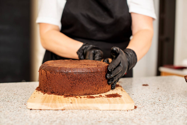 Pasta şefi, aşçı ya da siyah eldivenli fırıncı ve siyah mutfak önlüğü pasta yapıyor. Ev yapımı doğum günü pastası. Ev yapımı hamur işi, kek pişirme, hobi, küçük ev işi. - Fotoğraf, Görsel