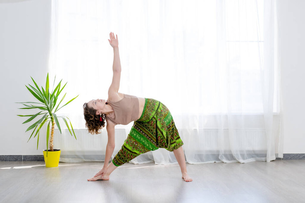 Jovem praticando ioga, de pé em Utthita Trikonasana exercício, pose triangular estendida - Foto, Imagem