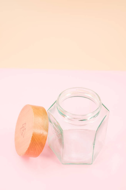 Empty glass jar with a wooden lid isolated on a pink background with copy space - Фото, изображение