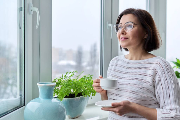 Middle aged beautiful woman with glasses with cup of coffee at home in winter autumn season - Fotografie, Obrázek