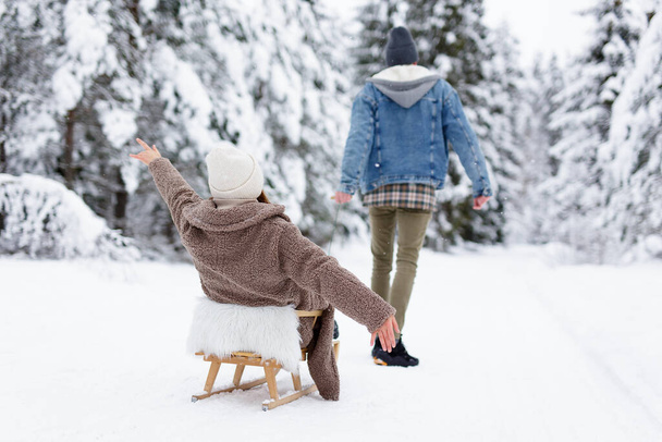 Вид сзади мужчины, тягающего санки с веселой женщиной в зимнем лесу - Фото, изображение