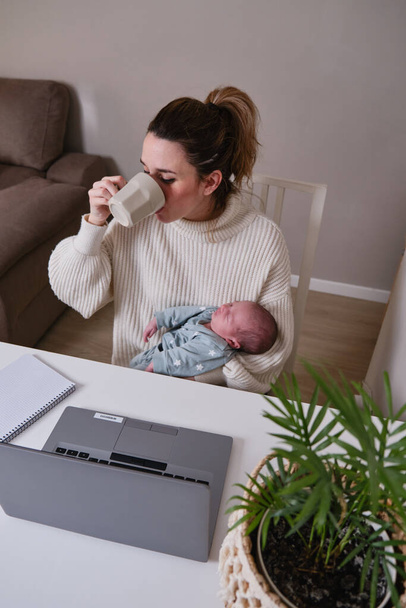 Мама з новонародженого Кавказу працює вдома з ноутбуком і випиває чашку кави. - Фото, зображення