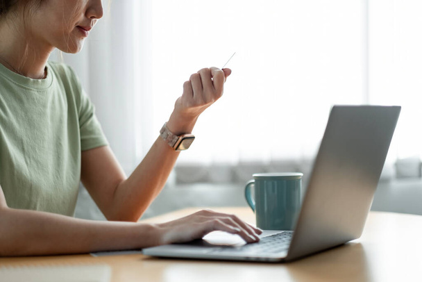Nahaufnahme einer Frau, die eine Kreditkarte in der Hand hält und die Computertastatur für Online-Einkäufe zu Hause benutzt. - Foto, Bild