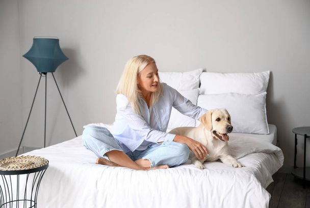 Donna matura con simpatico cane Labrador seduto sul letto a casa - Foto, immagini