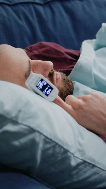 Nahaufnahme eines kranken Mannes, der mit einem Oximeter am Finger auf dem Sofa schläft - Foto, Bild