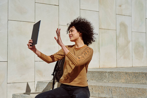 Attractive black girl waving a greeting while on a video call on her digital tablet outdoors during the day - Foto, Bild