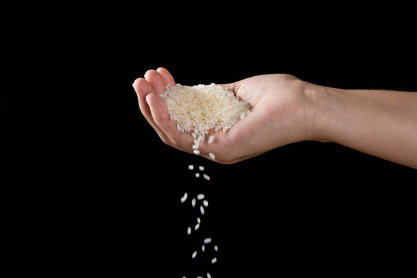 Hands dropping rice grain isolated on black background. - Foto, afbeelding