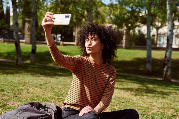 Carino giovane donna nera bronza mentre prende un selfie in un parco durante il giorno - Foto, immagini