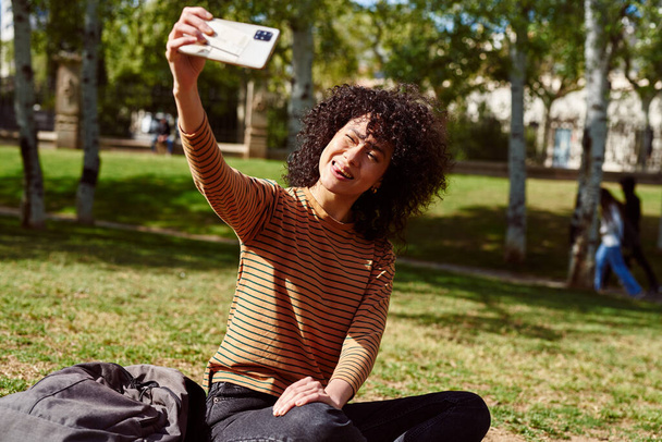 Attractive young woman smiling while taking a selfie in a park on a sunny day - Foto, immagini