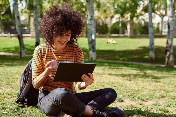 Cute young black woman celebrating while holding a tablet pc in a park during the day - Foto, afbeelding
