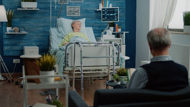 Вышедший на пенсию пациент с болезнью сидит на больничной койке - Фото, изображение