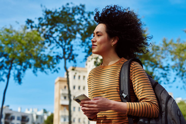 Ελκυστική νεαρή μαύρη γυναίκα που χρησιμοποιεί κινητό ενώ περπατάει στην ύπαιθρο κατά τη διάρκεια της ημέρας - Φωτογραφία, εικόνα