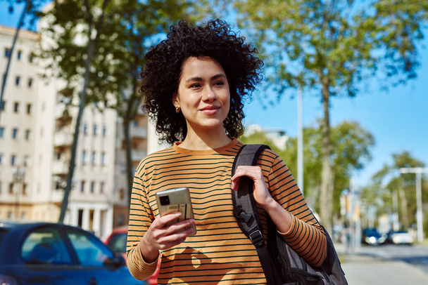 Привлекательная молодая черная женщина, пользующаяся сотовым телефоном, днем гуляя одна на улице. - Фото, изображение
