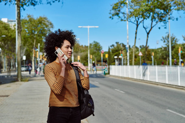 Cute young black woman speaking on the phone while standing by the roadside during the day - Fotó, kép