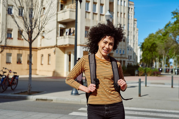 Smiling young black woman looking at the camera while standing with a backpack outdoors during the day - Photo, Image