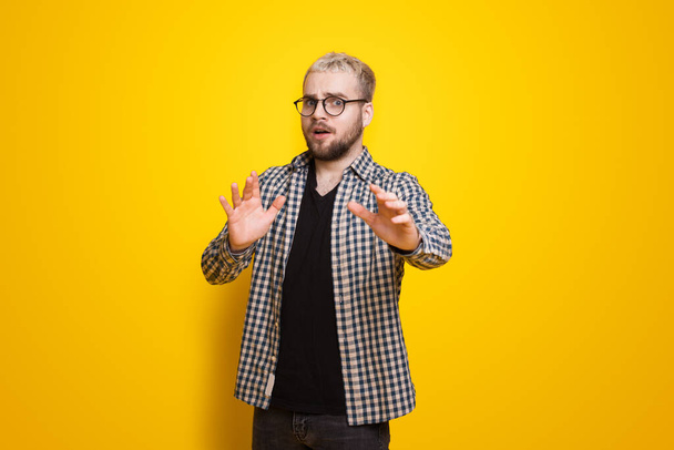 Trendy portrait of a blonde man gesturing fear for cover design. Handsome man. Fashion model. Gesturing no sign on yellow wall. - Photo, Image