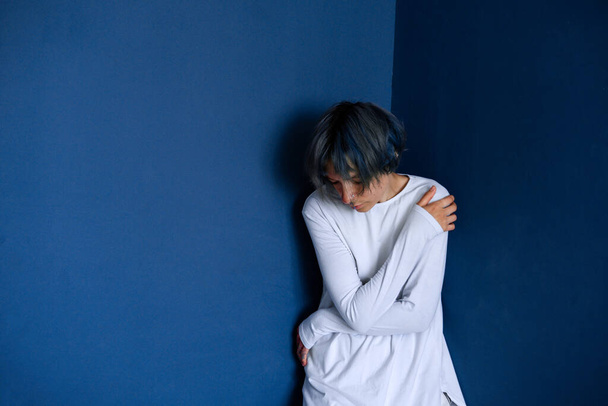 Ein junges Mädchen mit gesenktem Kopf steht zwischen blauen Wänden. Konzept der psychischen Erkrankungen. - Foto, Bild