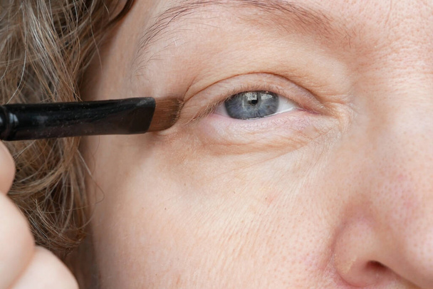 žena středního věku dělá korekční oční make-up pro korekci ochablých víček. Ptosis je svěšené horní víčko, líné oko. Kosmetika a obličejový koncept, detailní záběr - Fotografie, Obrázek