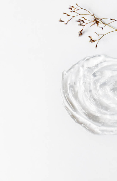 Texture gel de l'émulsion sur fond blanc. Crème transparente, petites fleurs sèches et espace de copie. - Photo, image