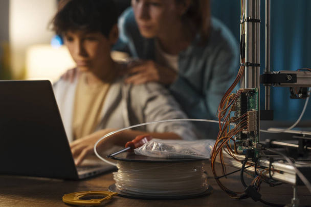 Teenagers learning 3D modeling and using a 3D printer, the boy is using a laptop and the girl is helping him - Fotografie, Obrázek
