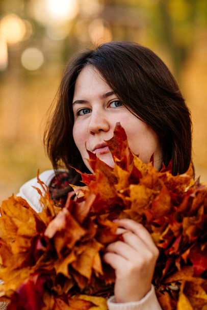 Portrait of beautiful romantic young woman with autumn yellow brown and red leaves, Close-up of a cute stylish girl in park holding golden leaves, Selective focus, natural light shot, vibrant colors. - Photo, Image