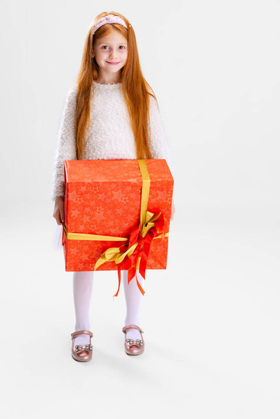 Full-length portrait of happy and delightful child, girl holding big present box isolated over white background - Photo, Image