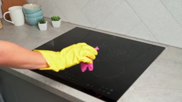 Καθαρισμός σόμπα εισαγωγής. Γυναίκα με κίτρινα λαστιχένια γάντια καθαρίζει επαγωγικές εστίες κουζίνας με σπινθήρα καθαρισμού και σφουγγάρι. Καθαρή συσκευή κουζίνας - Πλάνα, βίντεο