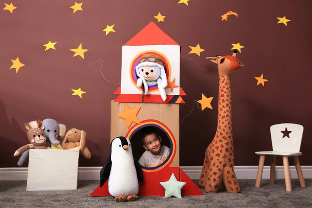 Cute little boy playing with cardboard rocket and toys at home. Child's room interior - Fotoğraf, Görsel