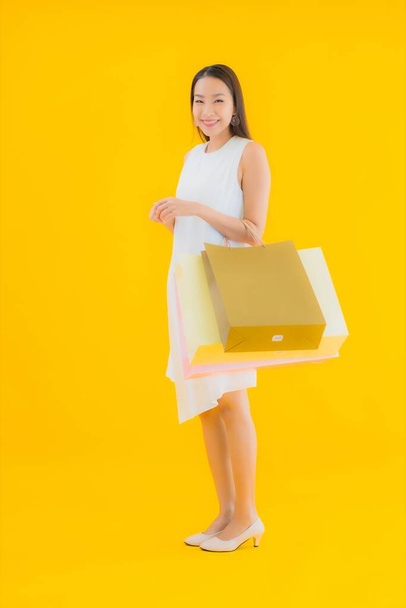Портрет красивая молодая азиатская женщина с сумкой из розничного магазина на желтом изолированном фоне - Фото, изображение