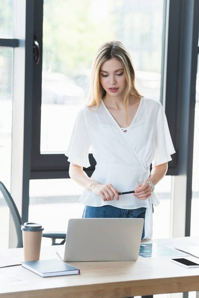 Молодая предпринимательница держит ручку рядом с устройствами на столе в офисе  - Фото, изображение