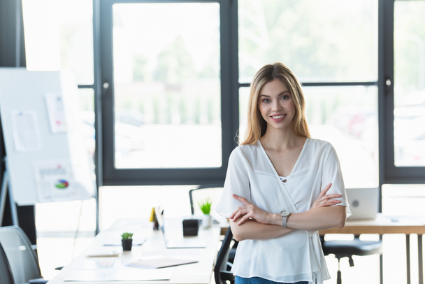 Young businesswoman with crossed arms smiling at camera in office  - Foto, afbeelding