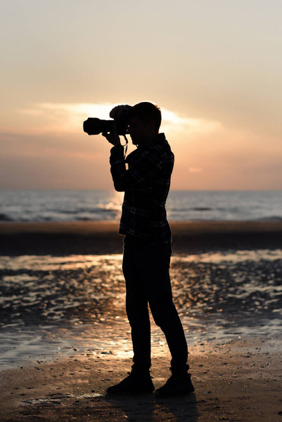mężczyzna fotograf kręci przed kamerą na plaży o zachodzie słońca - Zdjęcie, obraz