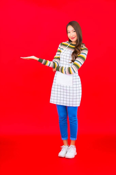Portrait beautiful young asian woman wear apron on red background - Photo, Image