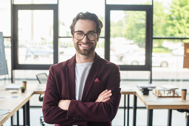 Young smiling businessman in eyeglasses looking at camera in blurred office  - Fotó, kép