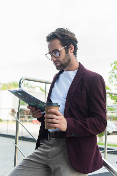 Businessman in formal wear and eyeglasses holding coffee to go and paper outdoors  - Photo, image