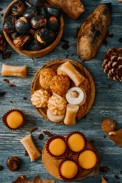 high angle view of a gray rustic table with some roasted chestnuts and some different confections eaten in Spain on All Saints Day, such as Panellets, Huesos de Santo or Yemas de Santa Teresa - Photo, Image