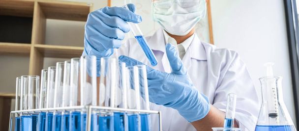 Ženský vědecký výzkumník nebo lékař pracující v laboratoři o antiretrovirové koronavirové covid19 výzkumná vyšetření pomocí zkumavek a roztoku modré kapaliny. - Fotografie, Obrázek